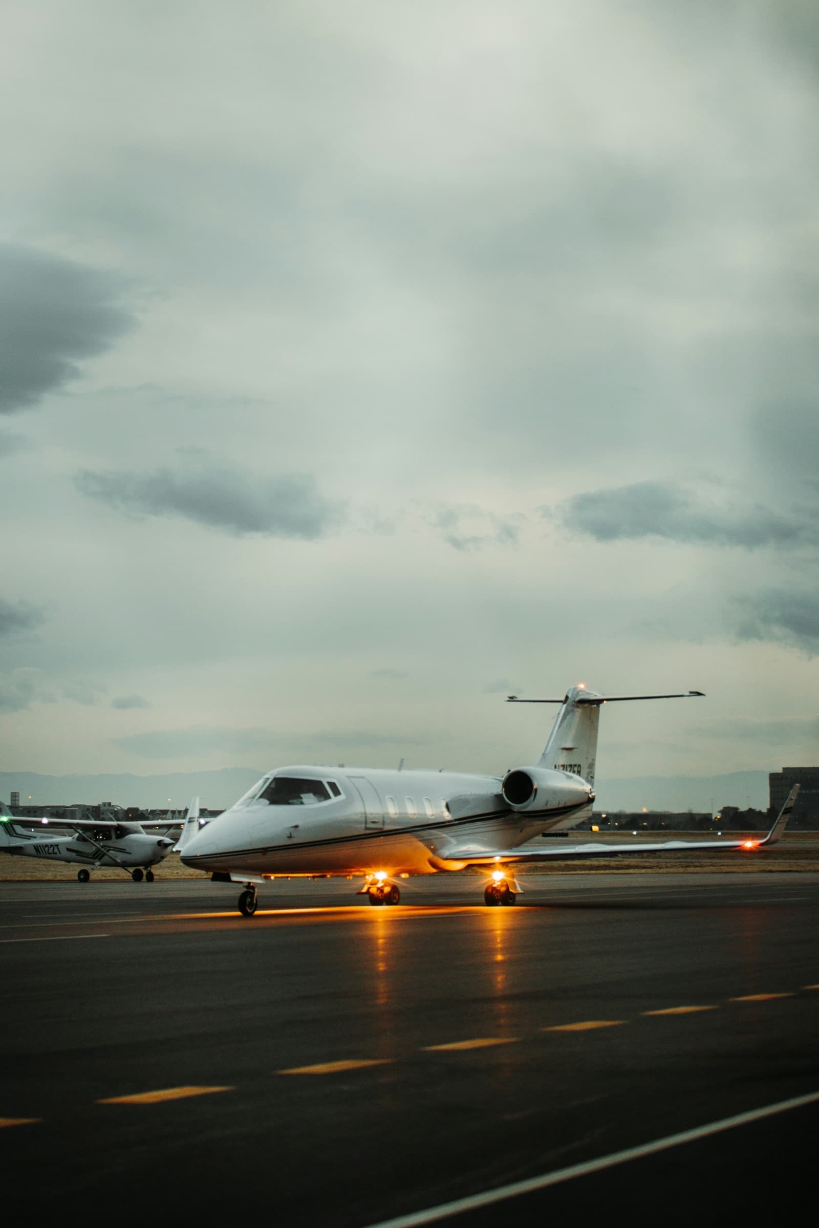A business jet taxiing at dusk with its landing lights reflecting on the wet tarmac.
