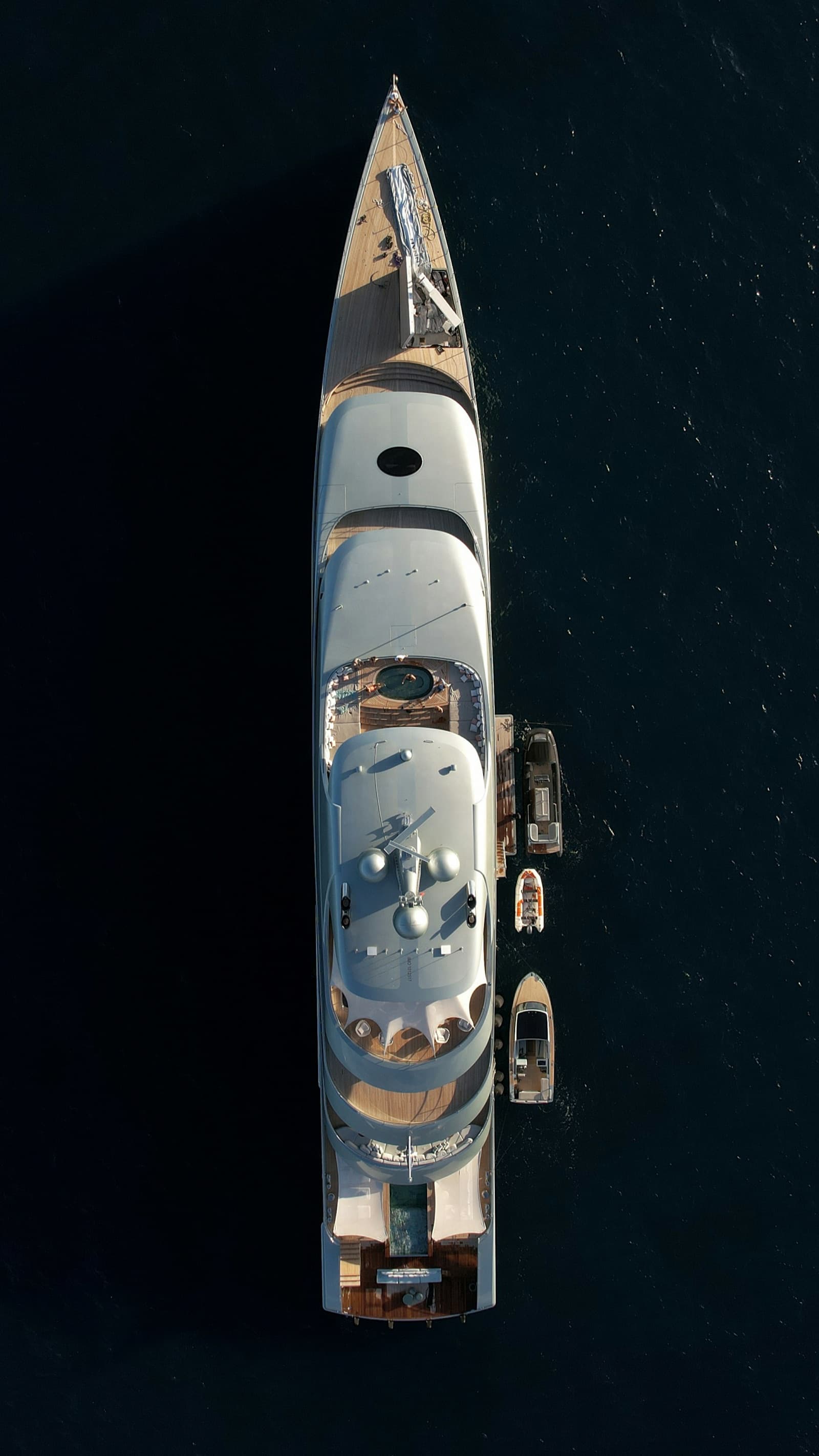 A superyacht at anchor seen from directly above, with tenders alongside on dark water.